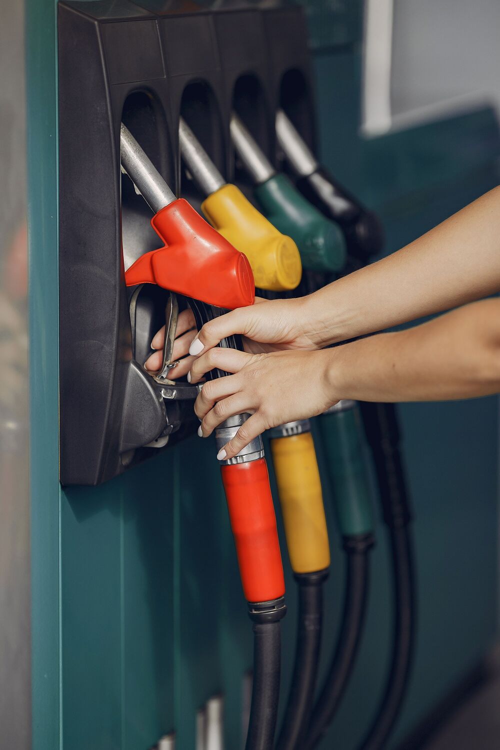 Hands lifting a fuel nozzle from a multi-grade pump